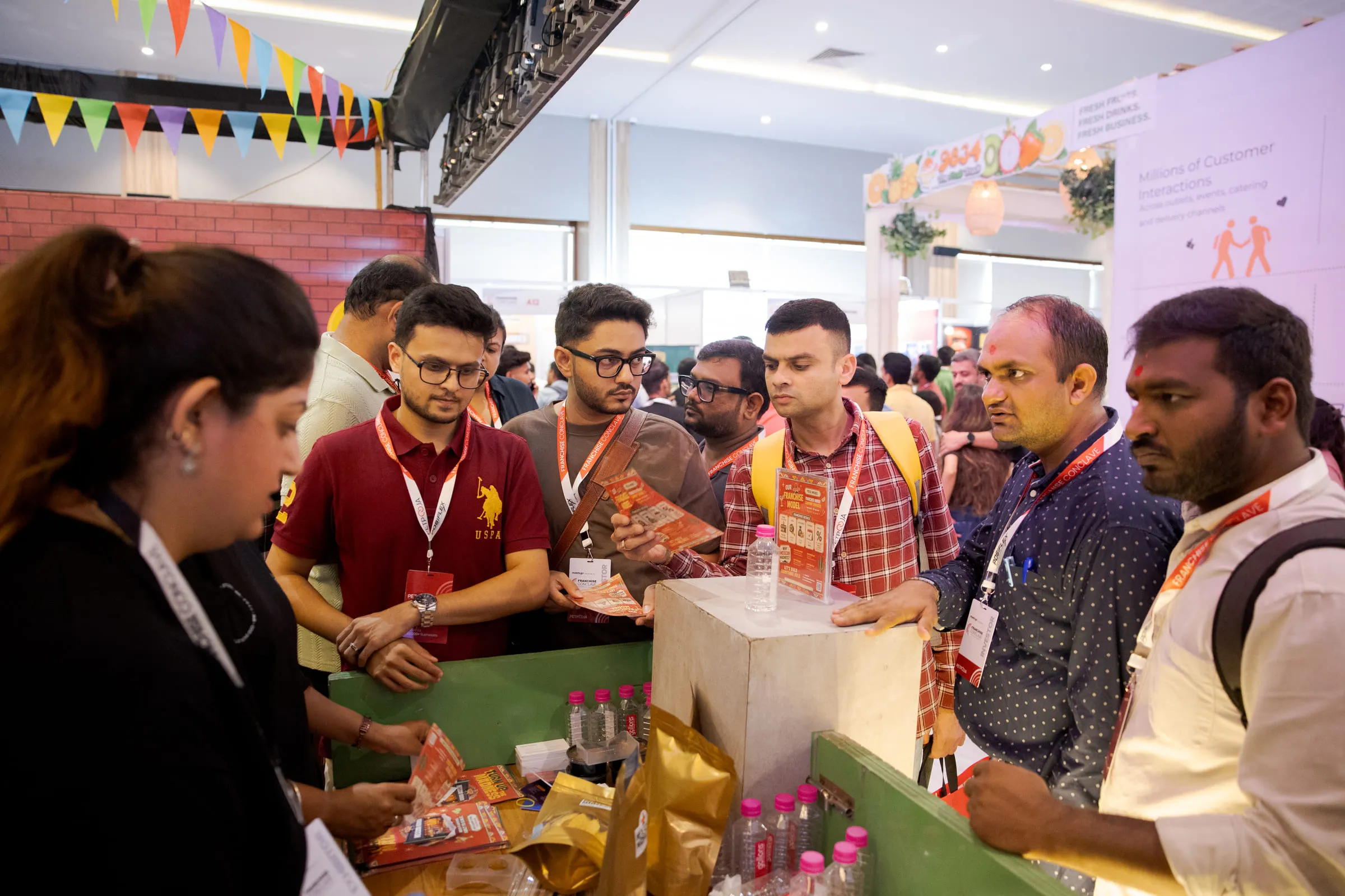 A crowd of investors gathered around a stall, wearing Franchise Conclave lanyards