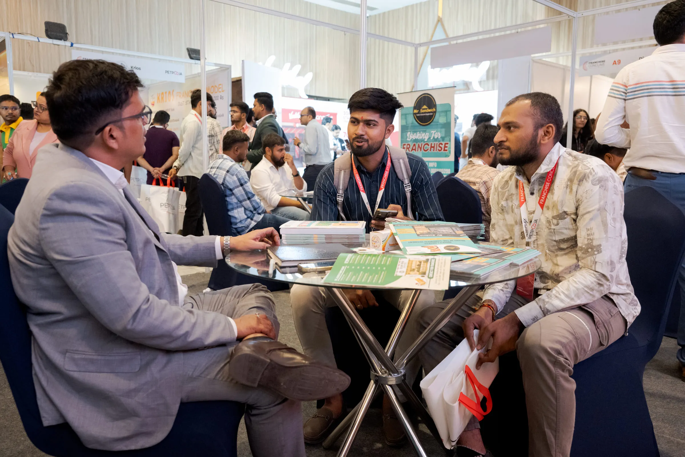 Three investors in conversation with an exhibitor across a table on the Conclave floor